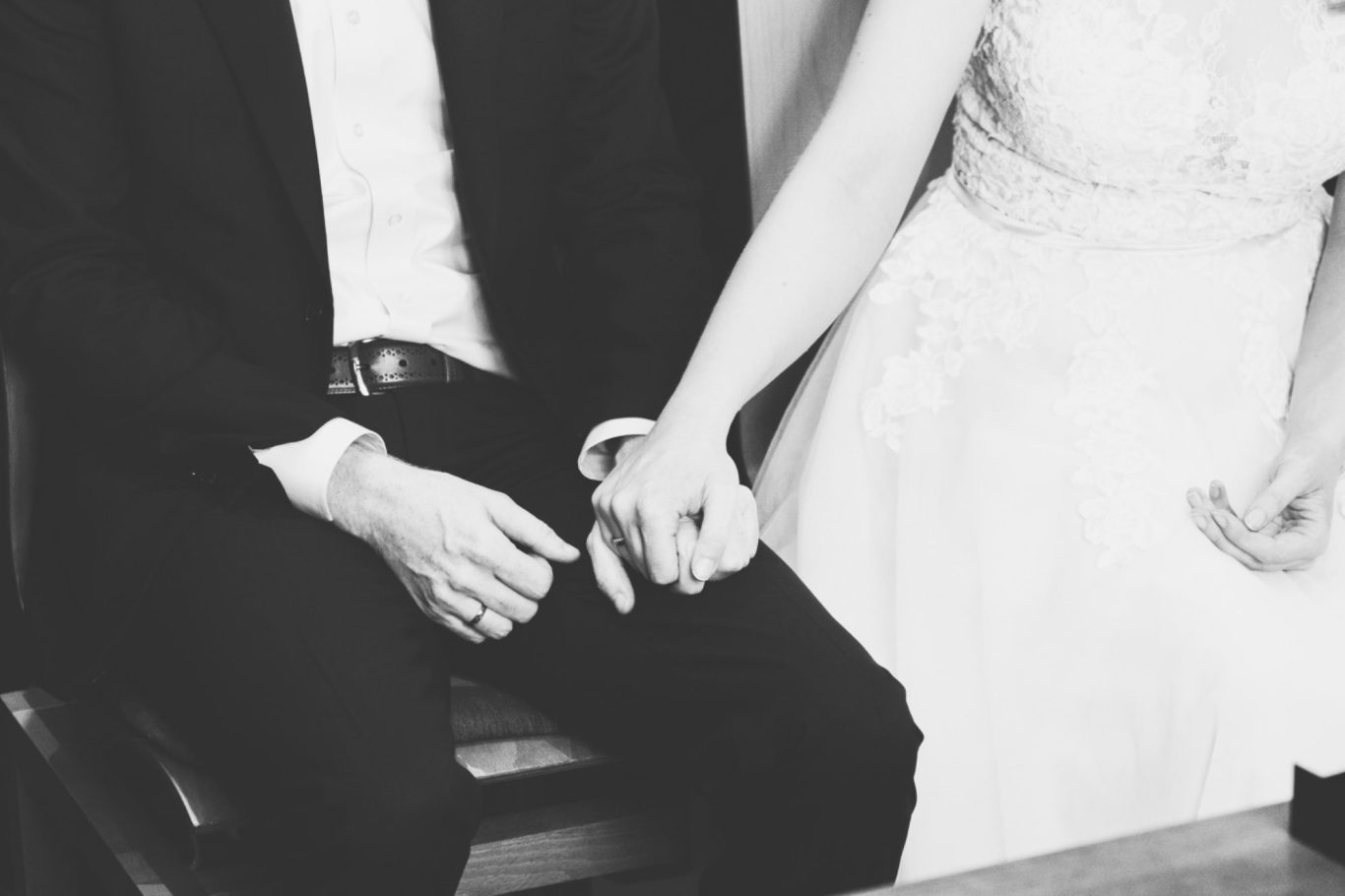 Hochzeitsfotografie Händchen haltendes Paar, das an einem Tisch sitzt, mit formeller Kleidung.