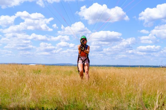 Person in Sportbekleidung läuft durch hohes Gras unter einem blauen Himmel mit Wolken.